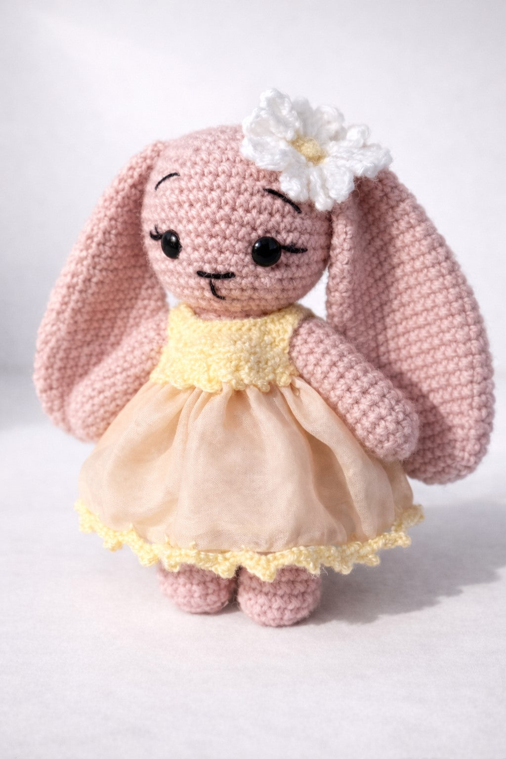 Crocheted bunny toy with a yellow dress and white flower on a light background