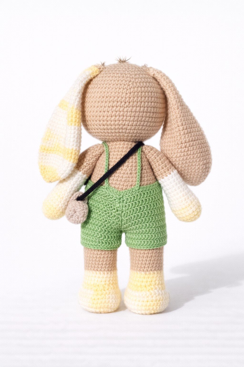 Crocheted Bunny with bunny ears and green overalls on a white background