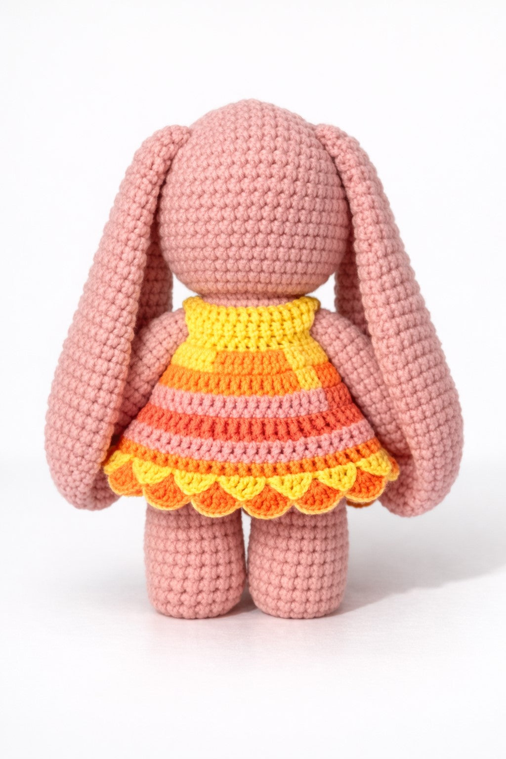Crocheted pink bunny with a colorful dress on a white background