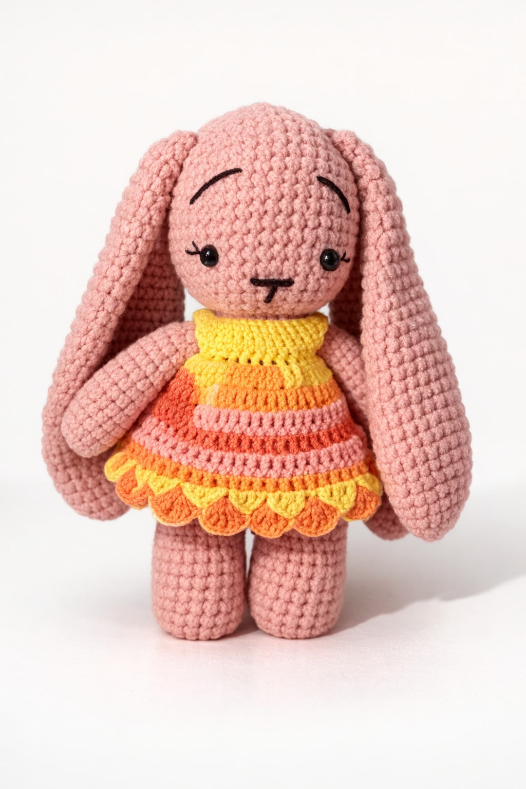 Crocheted pink bunny with a colorful dress on a white background