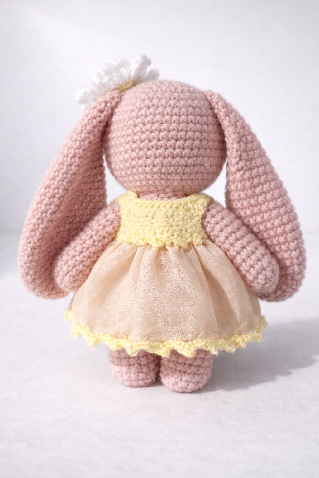 Pink crochet bunny with a yellow dress on a white background