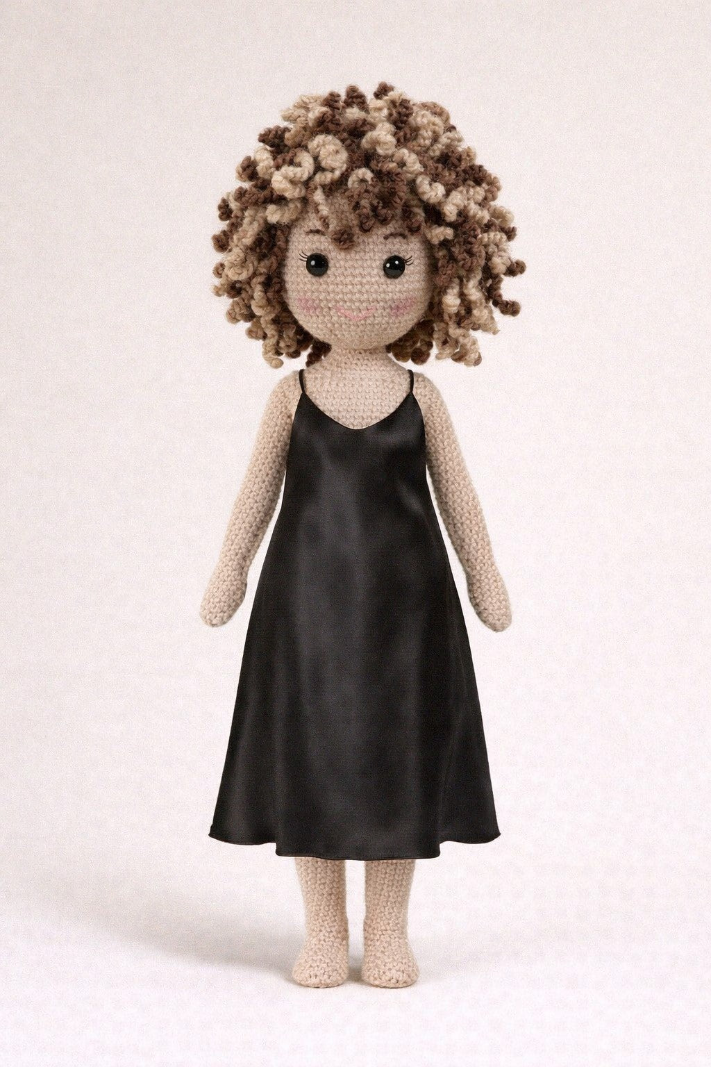 Crocheted doll with curly hair wearing a black dress on a light background