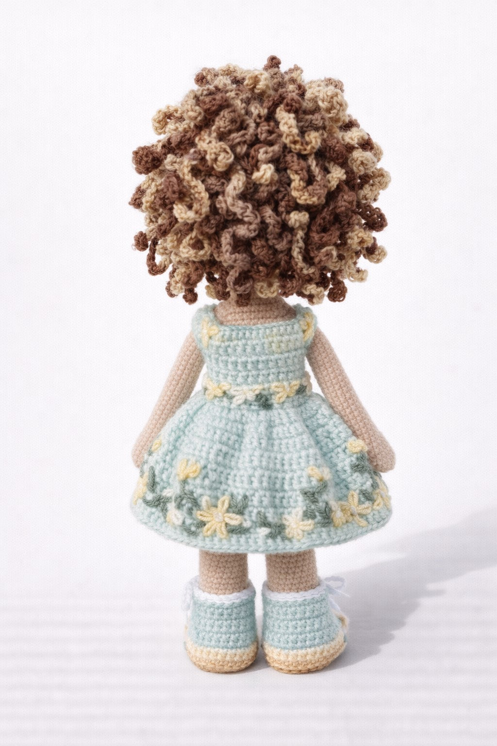 Crocheted doll with curly hair wearing a light blue dress on a white background