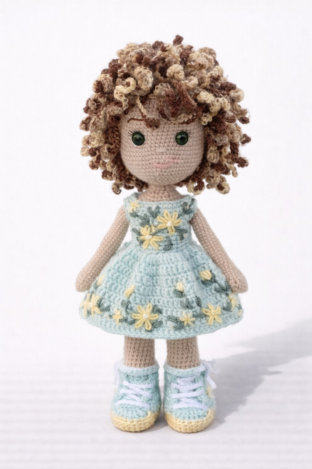 Crocheted doll with curly hair wearing a floral dress on a white background
