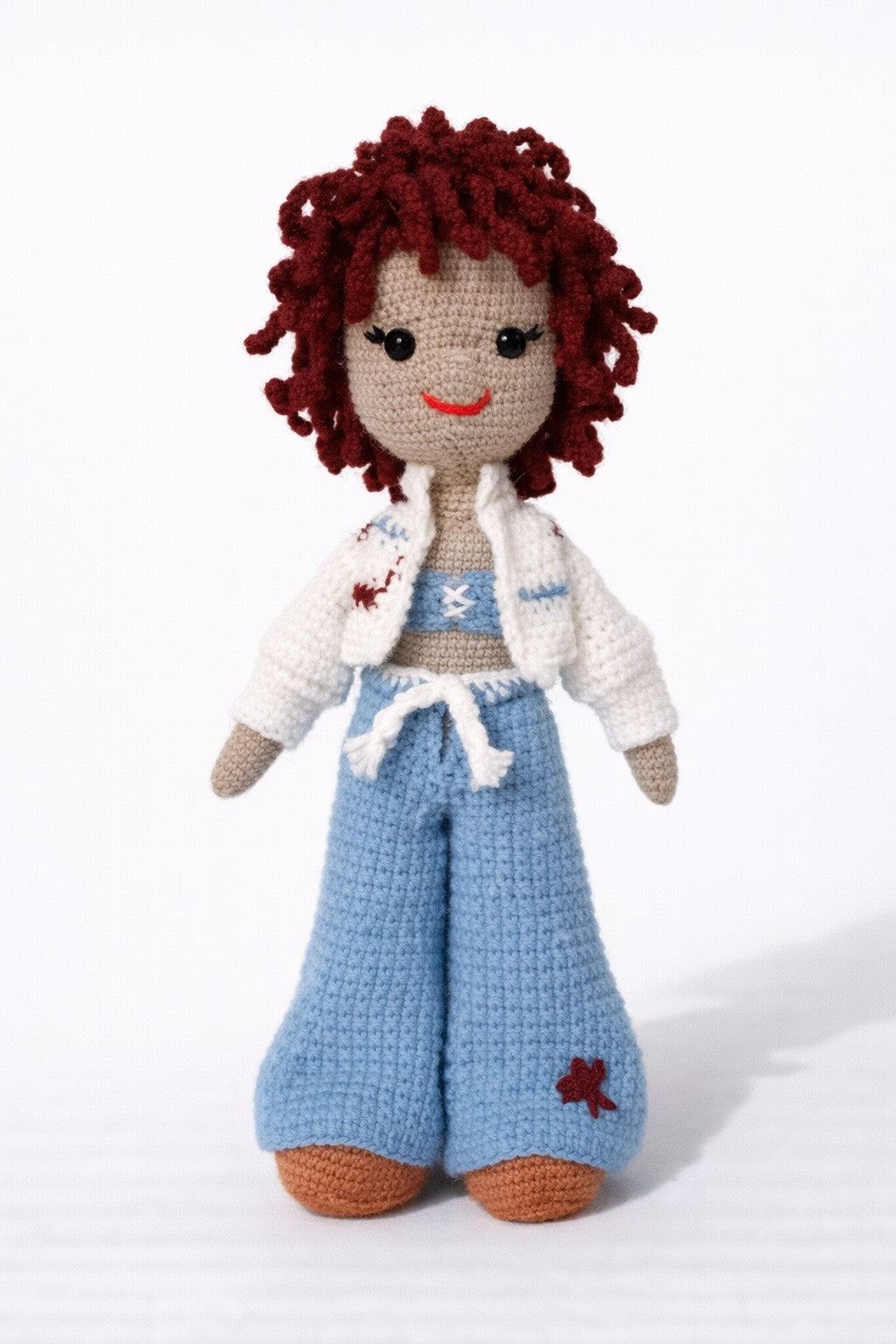 Crocheted doll with red hair, white jacket, and blue pants on a white background