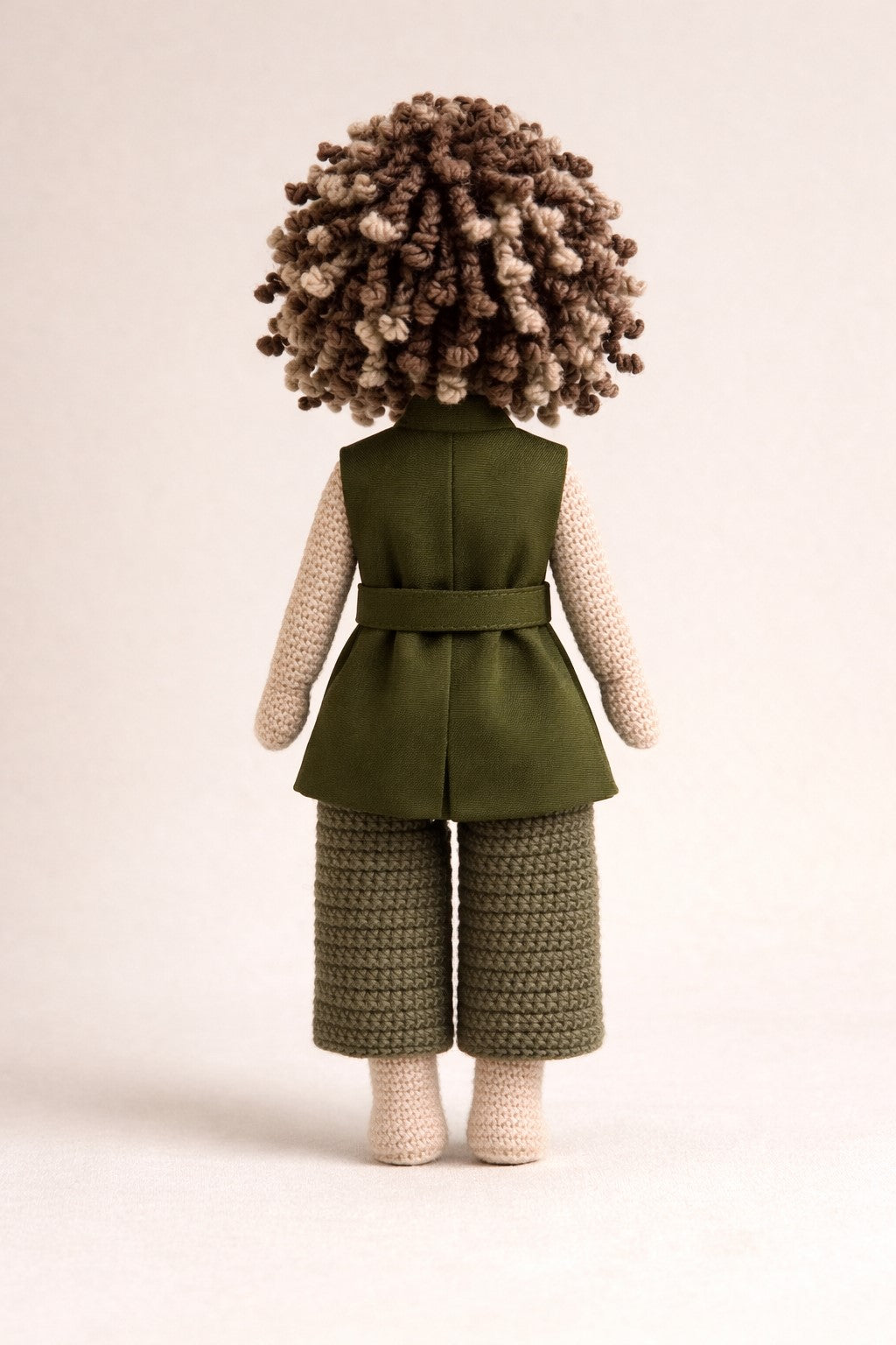 Crocheted doll wearing a green outfit with a vest on a beige background