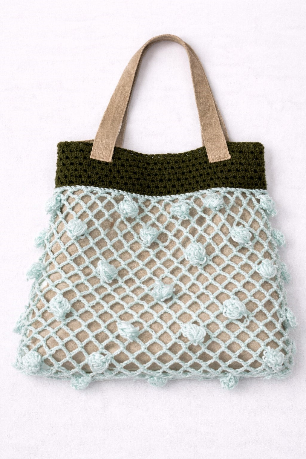 Crocheted bag with green top section and beige bottom section on a white background