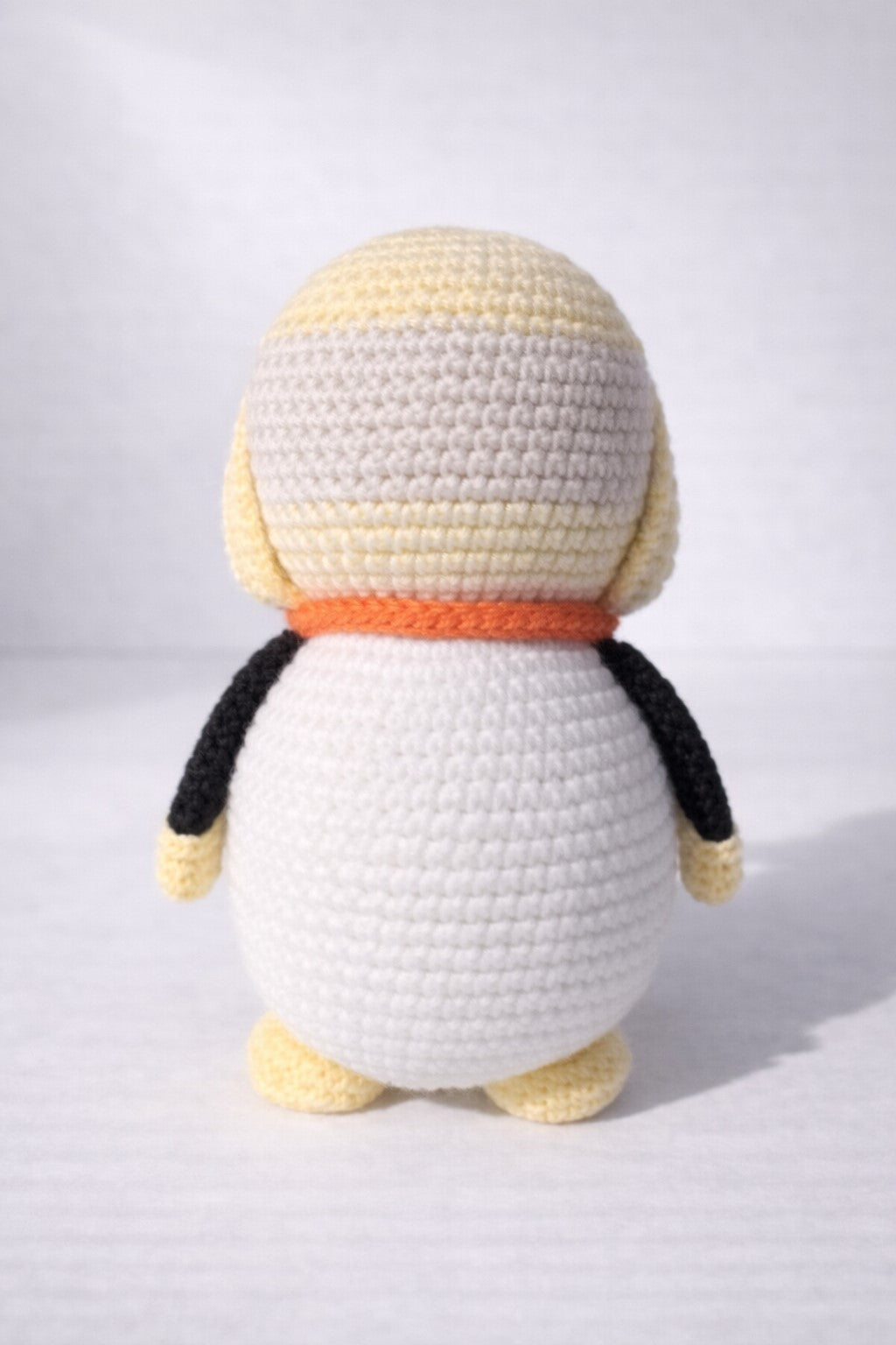 Crocheted penguin doll with a white body, black wings, and a yellow beak on a light gray background