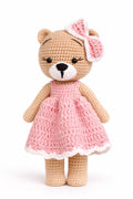 Crocheted teddy bear in a pink dress with a matching headband on a white background
