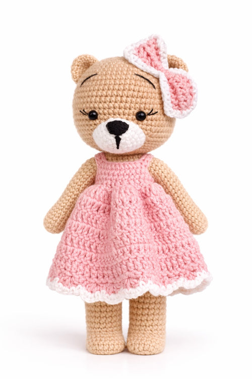 Crocheted teddy bear in a pink dress with a matching headband on a white background