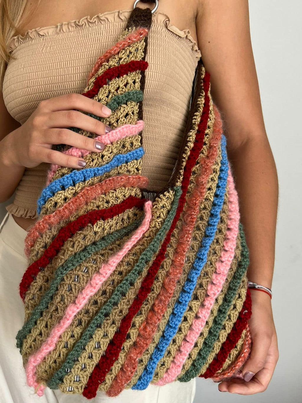 Multicolored striped crocheted bag held by a person against a neutral background