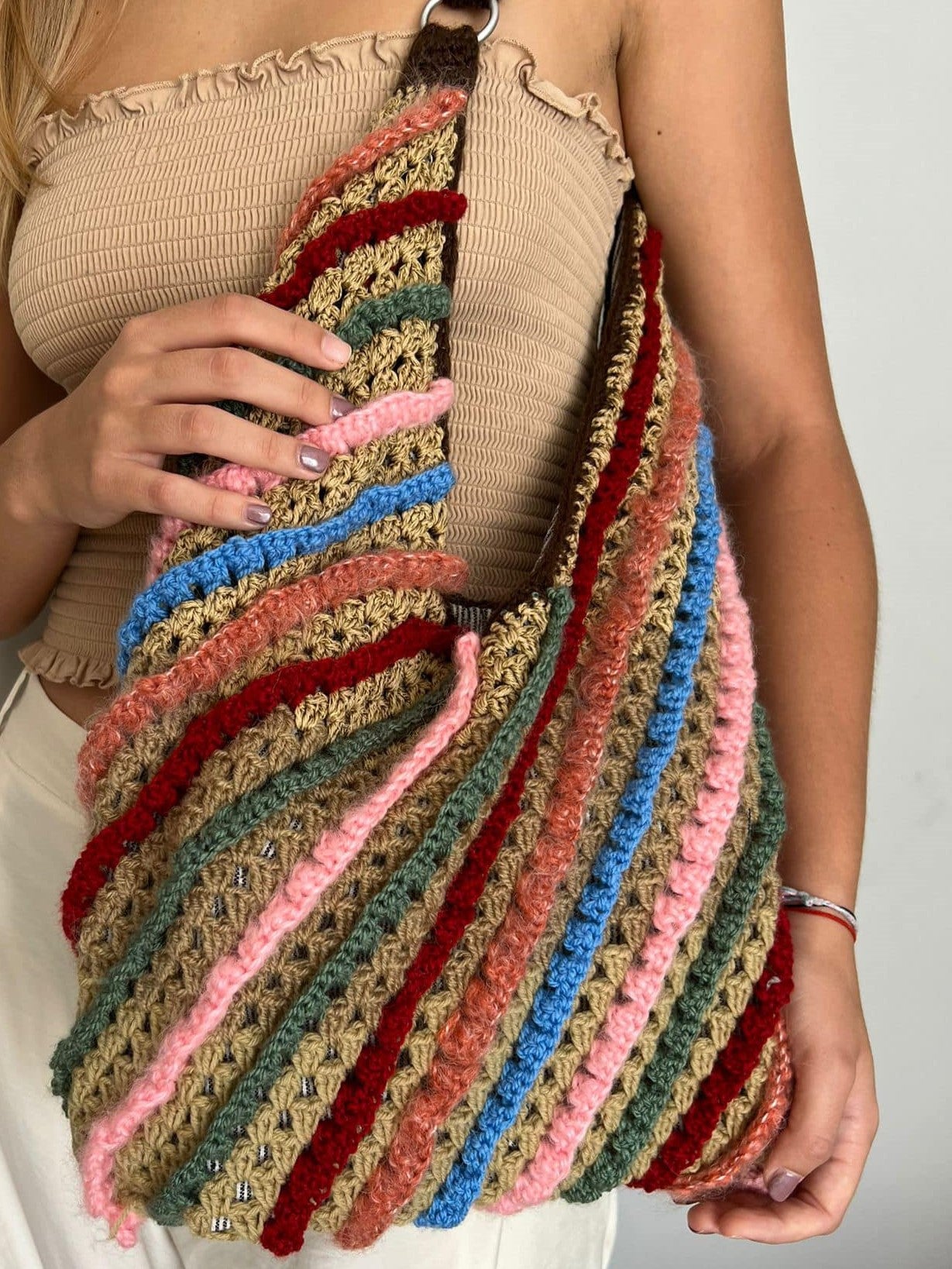 Multicolored striped crocheted bag held by a person against a neutral background