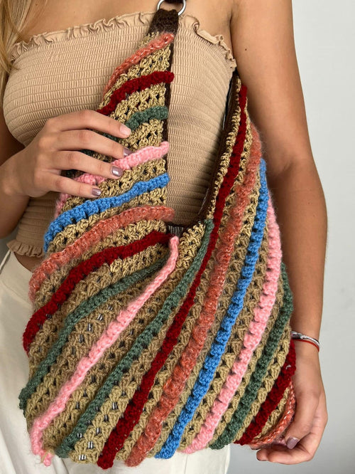 Multicolored striped crocheted bag held by a person against a neutral background