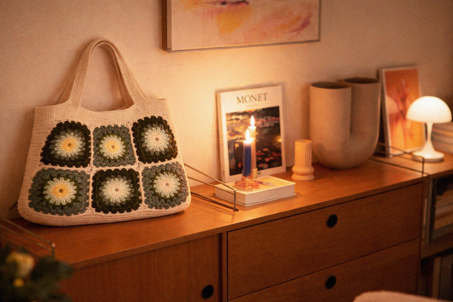 Handmade floral crochet bag on a wooden surface with books and decor items.
