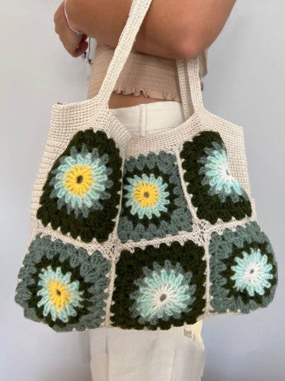 Crocheted bag with a floral pattern held by a person against a plain background