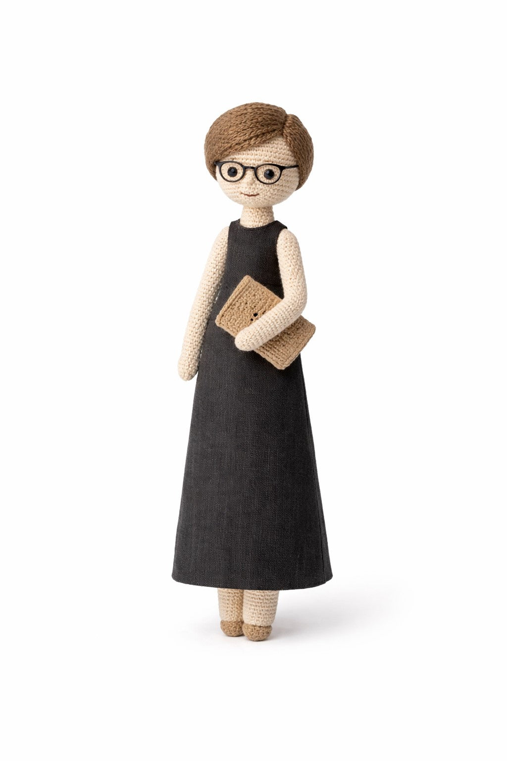Knitted doll with glasses and a black dress holding a book on a white background