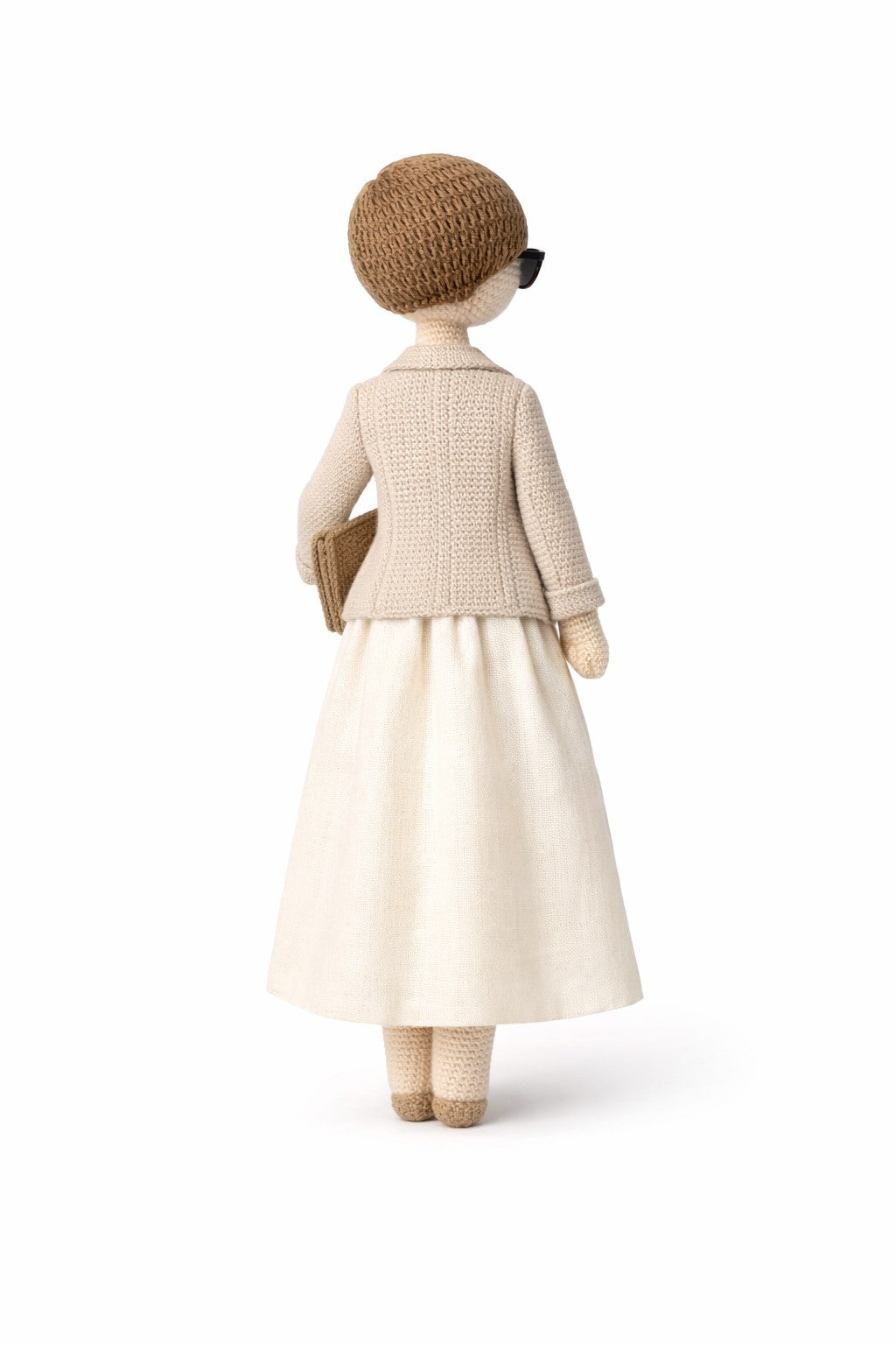 Crocheted figure wearing a beige outfit on a white background