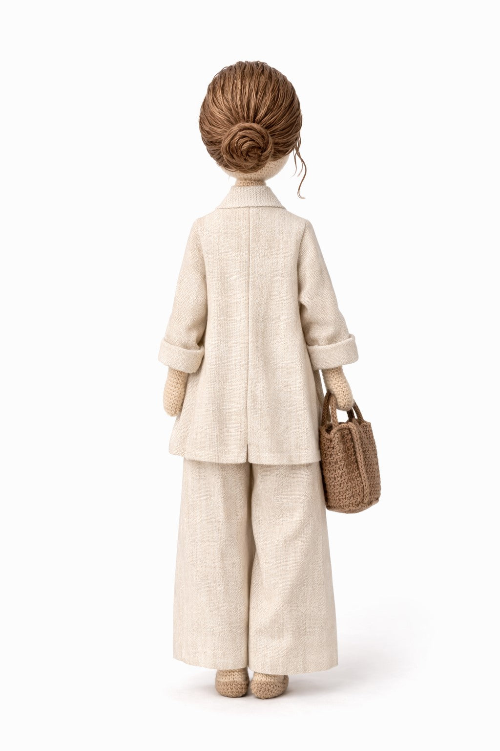 Crocheted figure wearing a beige outfit with a woven bag on a white background